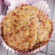 A close-up of a baked muffin in a crinkled paper liner, showing a golden-brown top with visible chunks of fruit or nuts.