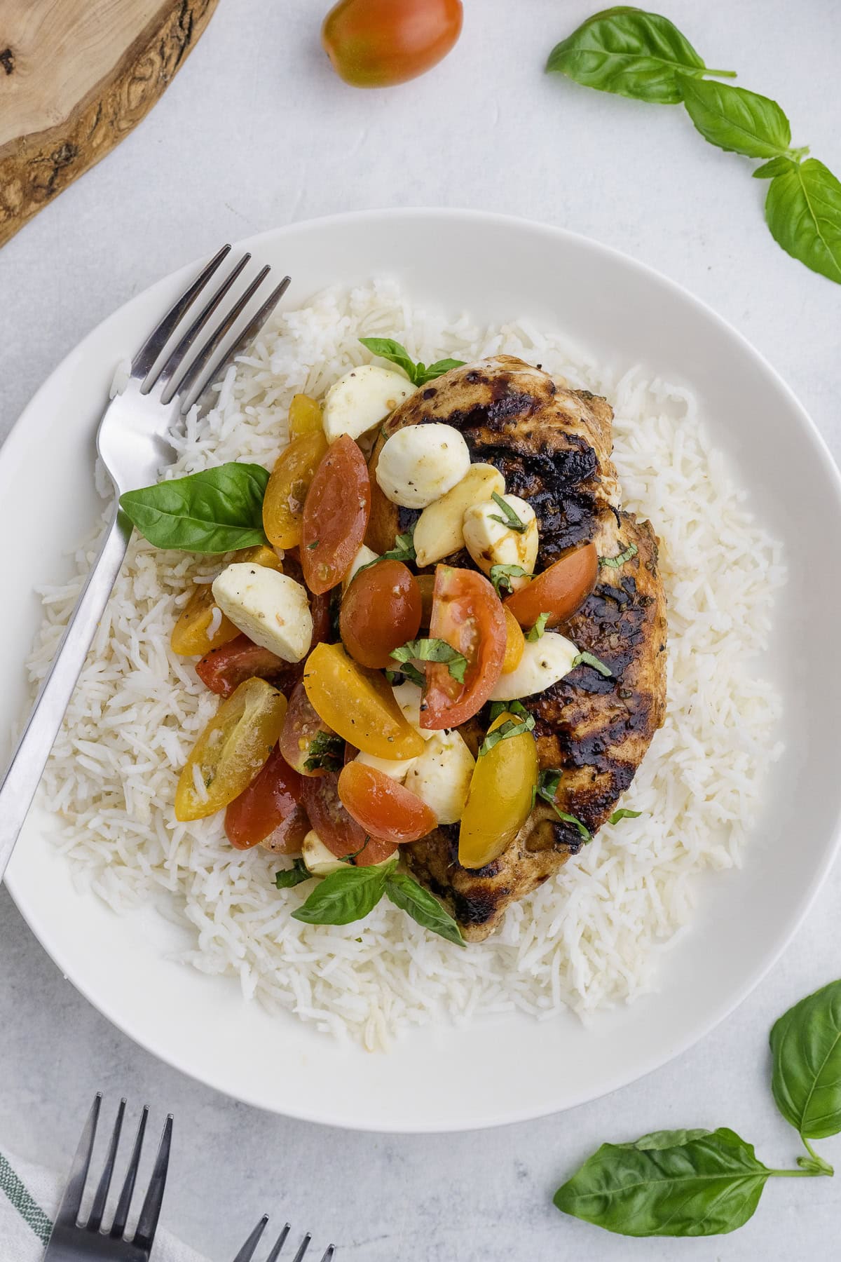 A plate of grilled chicken breast on white rice, topped with a tomato, mozzarella, and basil salad. A fork rests on the plate.