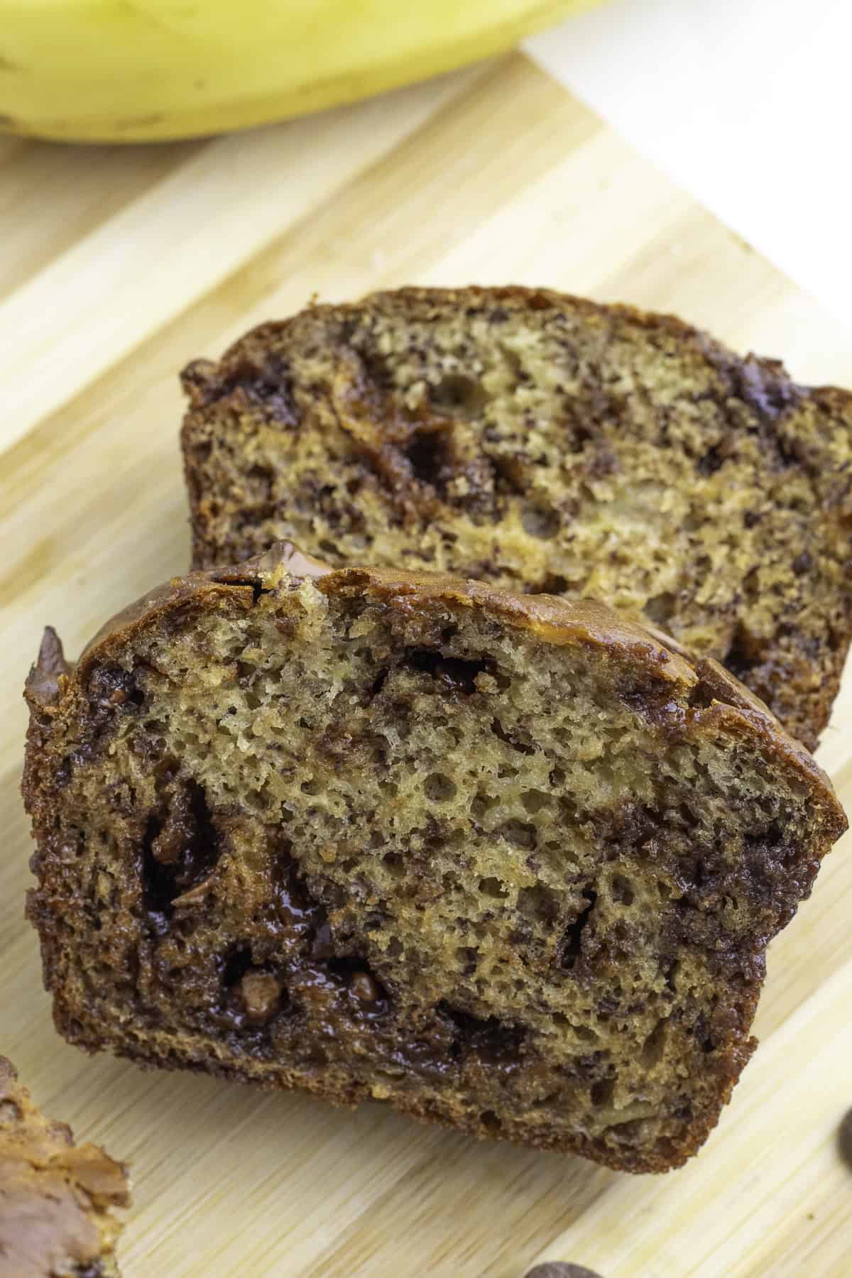 Two slices of banana bread with visible chocolate chips, placed on a wooden cutting board.
