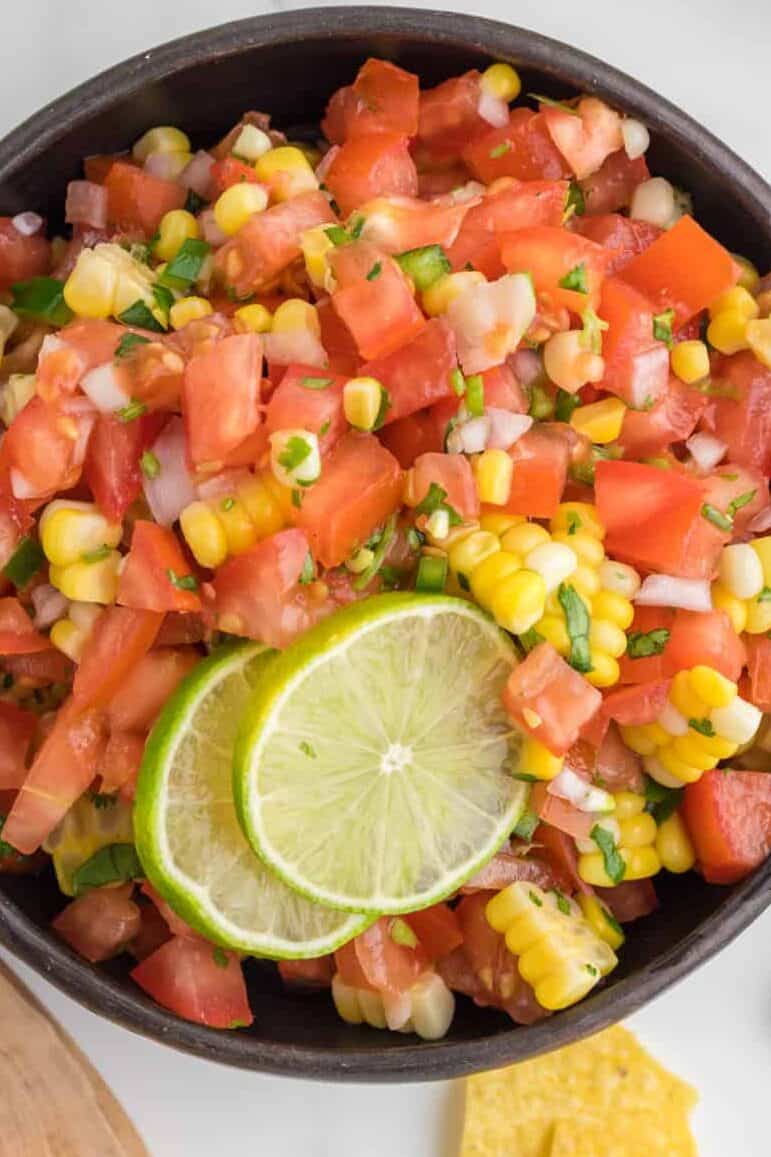 corn pico de gallo in a serving bowl with slice of lime on too. Top view.