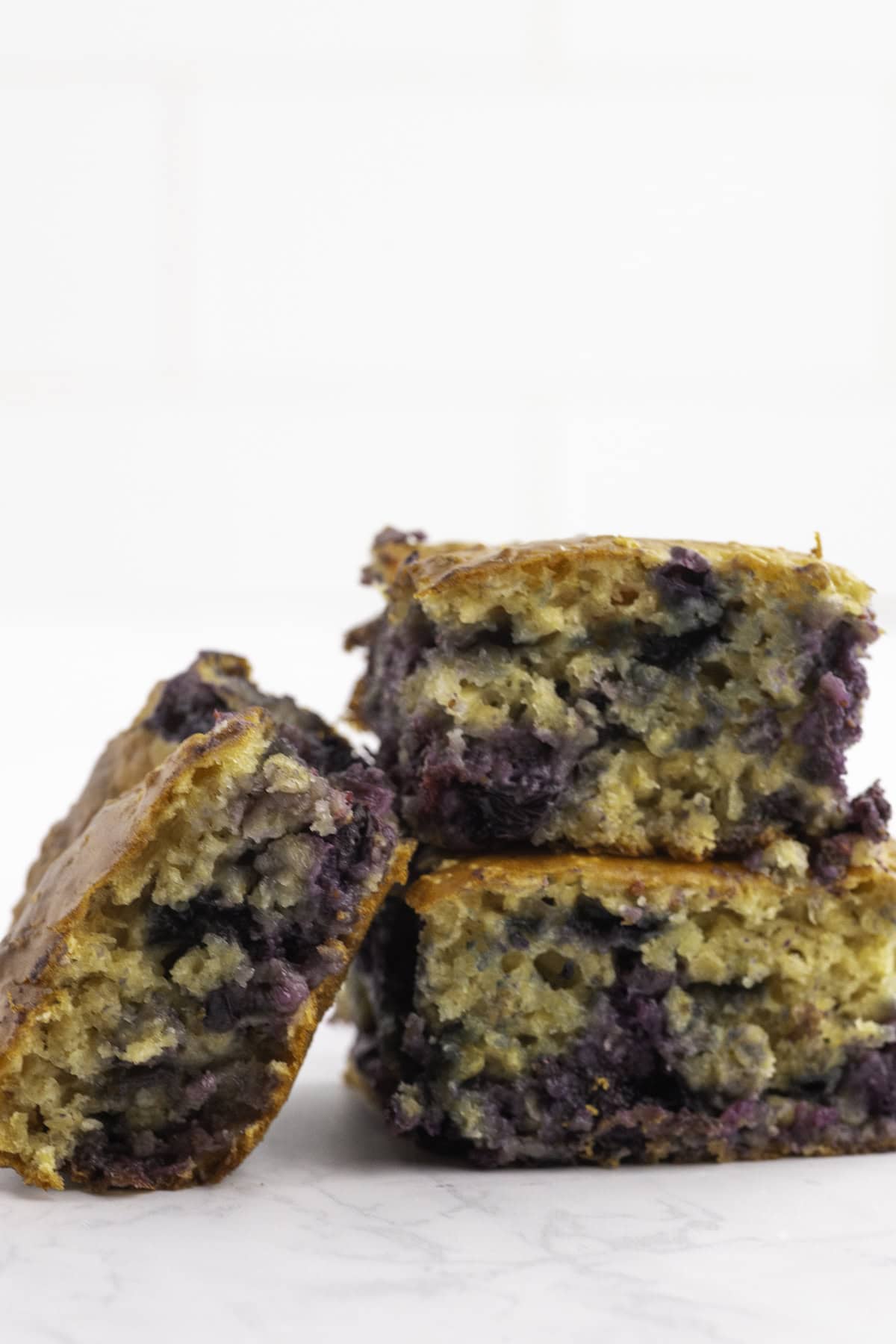 Three square pieces of blueberry yogurt are stacked on a white surface with a white background.