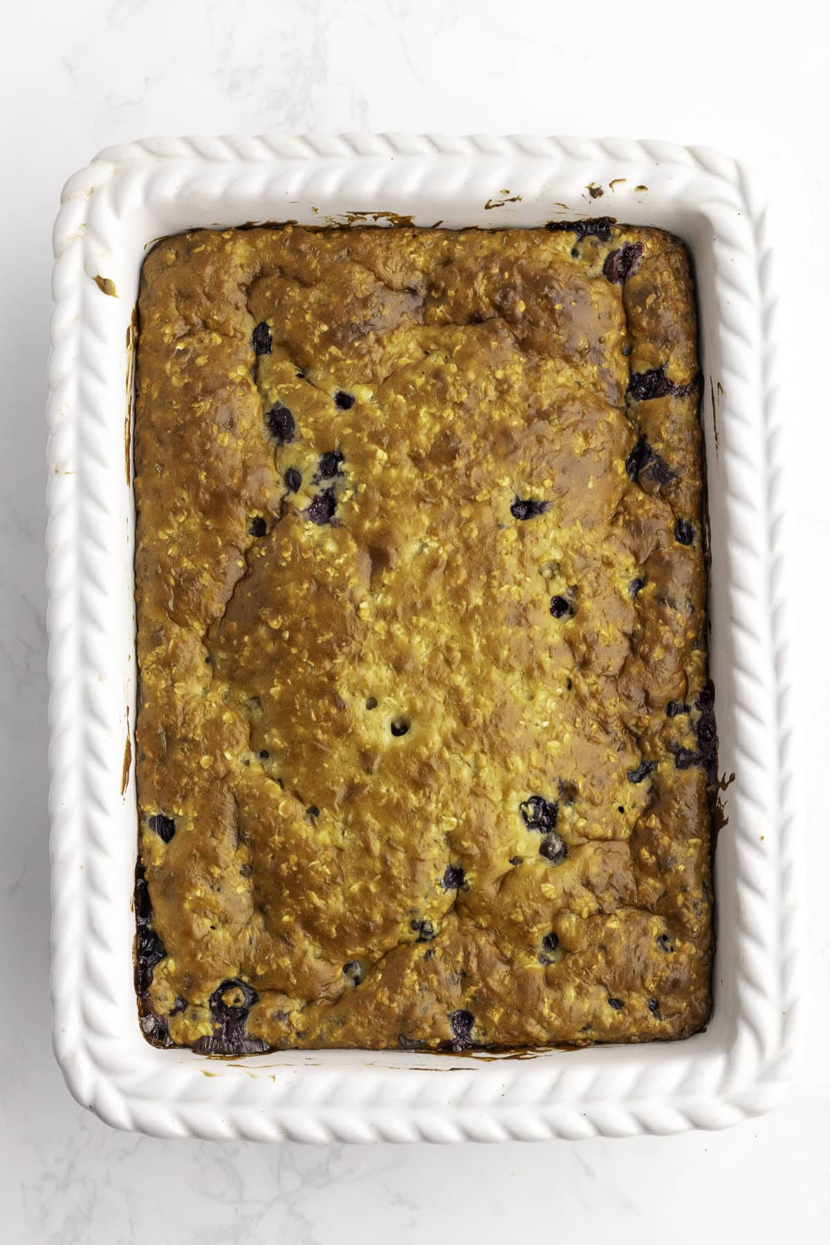 A rectangular white baking dish filled with a golden-brown baked blueberry bread.