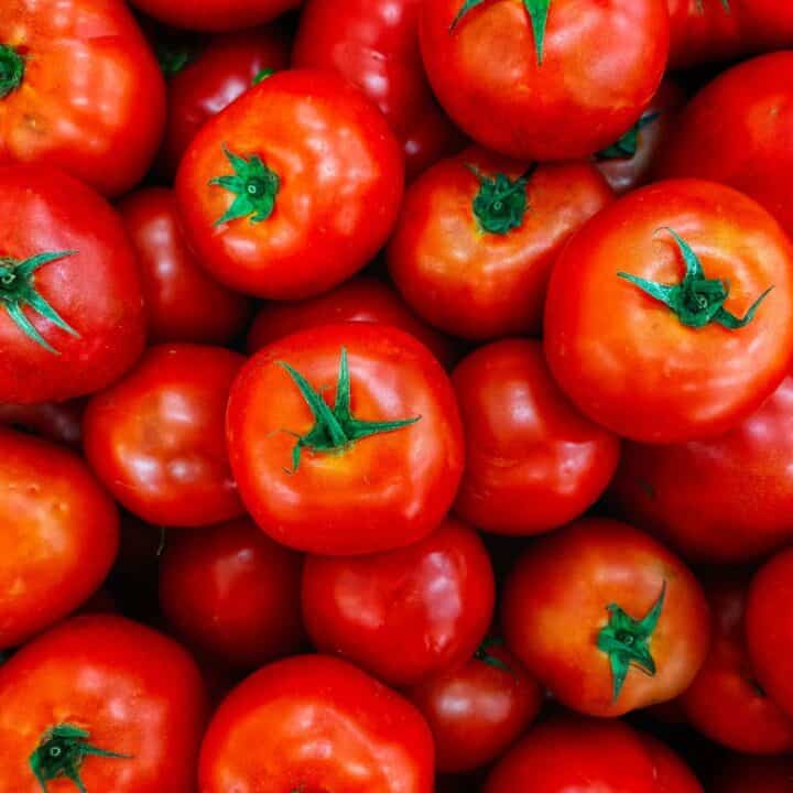 Vue rapprochée d'un tas de tomates rouges fraîches avec des tiges vertes.
