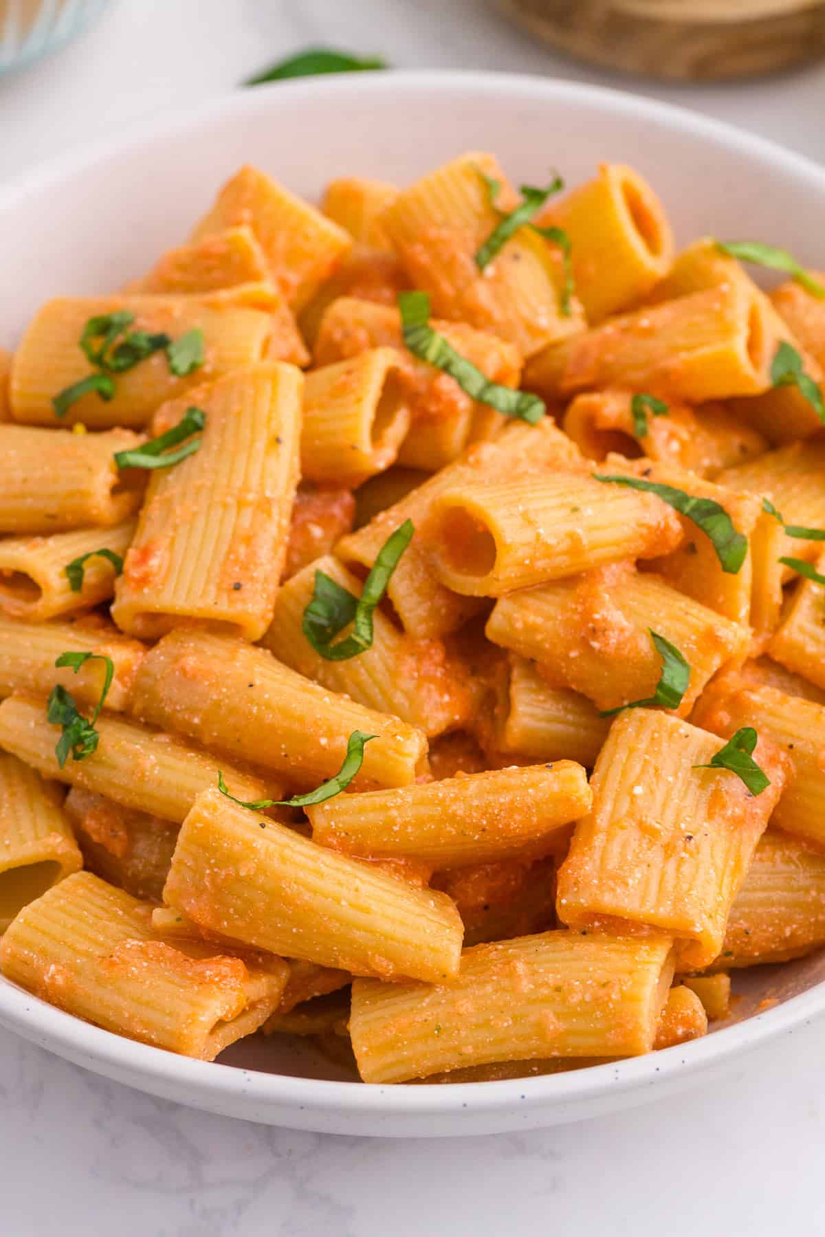 A bowl of rigatoni pasta coated in a creamy tomato sauce, garnished with chopped fresh basil.