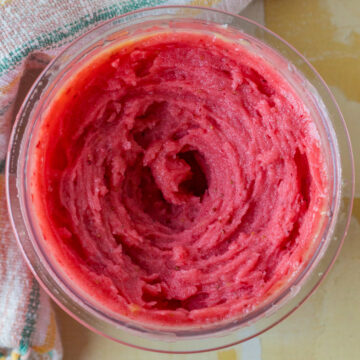 A bowl of red, textured frozen sorbet with a spiral pattern on the surface, next to a towel.