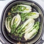 Des morceaux de bok choy coupés en deux sont disposés dans le panier d'une friteuse, apparaissant partiellement cuits avec des feuilles flétries.