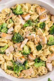 A skillet filled with cheese tortellini, broccoli florets, and pieces of grilled chicken, garnished with chopped herbs.
