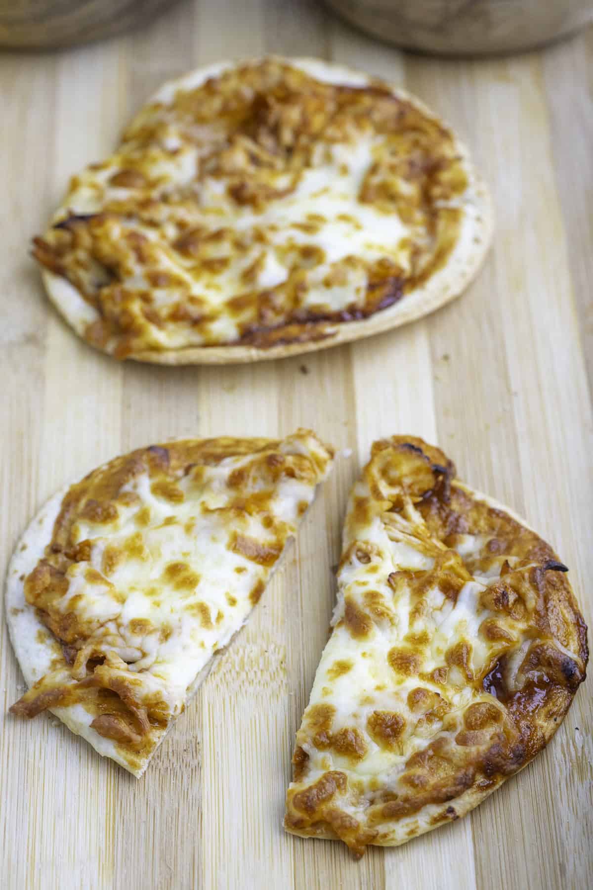 Two small, round pizzas with melted cheese sit on a wooden surface; one pizza is whole, the other is cut in half.