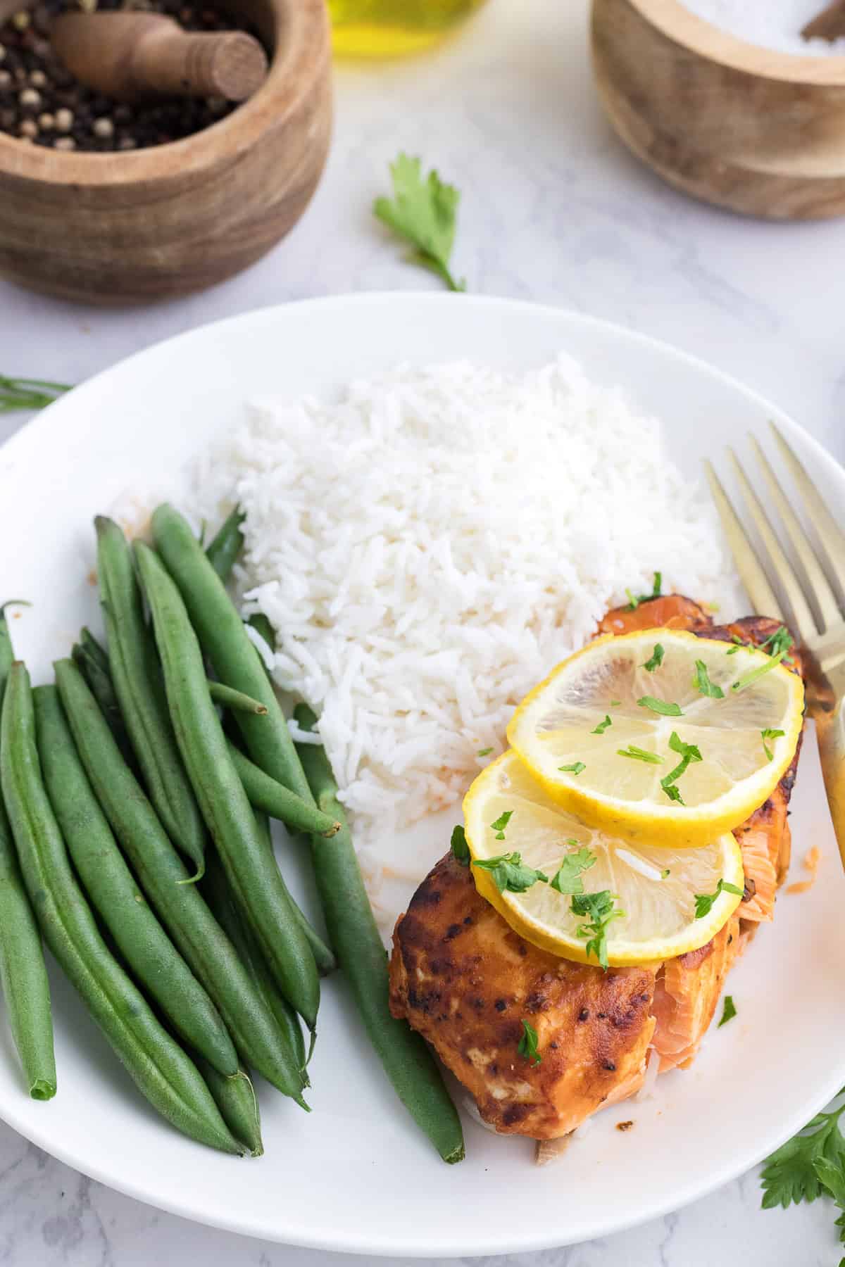 Une assiette avec du riz blanc, des haricots verts et un filet de saumon cuit au four, garni de tranches de citron et d'herbes, avec une fourchette à côté.