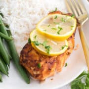 Filet de saumon grillé garni de tranches de citron, servi avec du riz blanc et des haricots verts sur une assiette blanche avec une fourchette dorée.