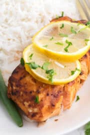 A plate of grilled salmon topped with lemon slices, served with white rice and green beans, with a gold fork on the side.