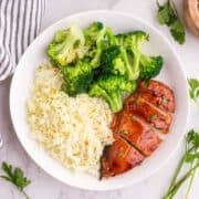 A white plate with steamed broccoli, white rice, and sliced Air Fryer BBQ Chicken Breast topped with glaze.
