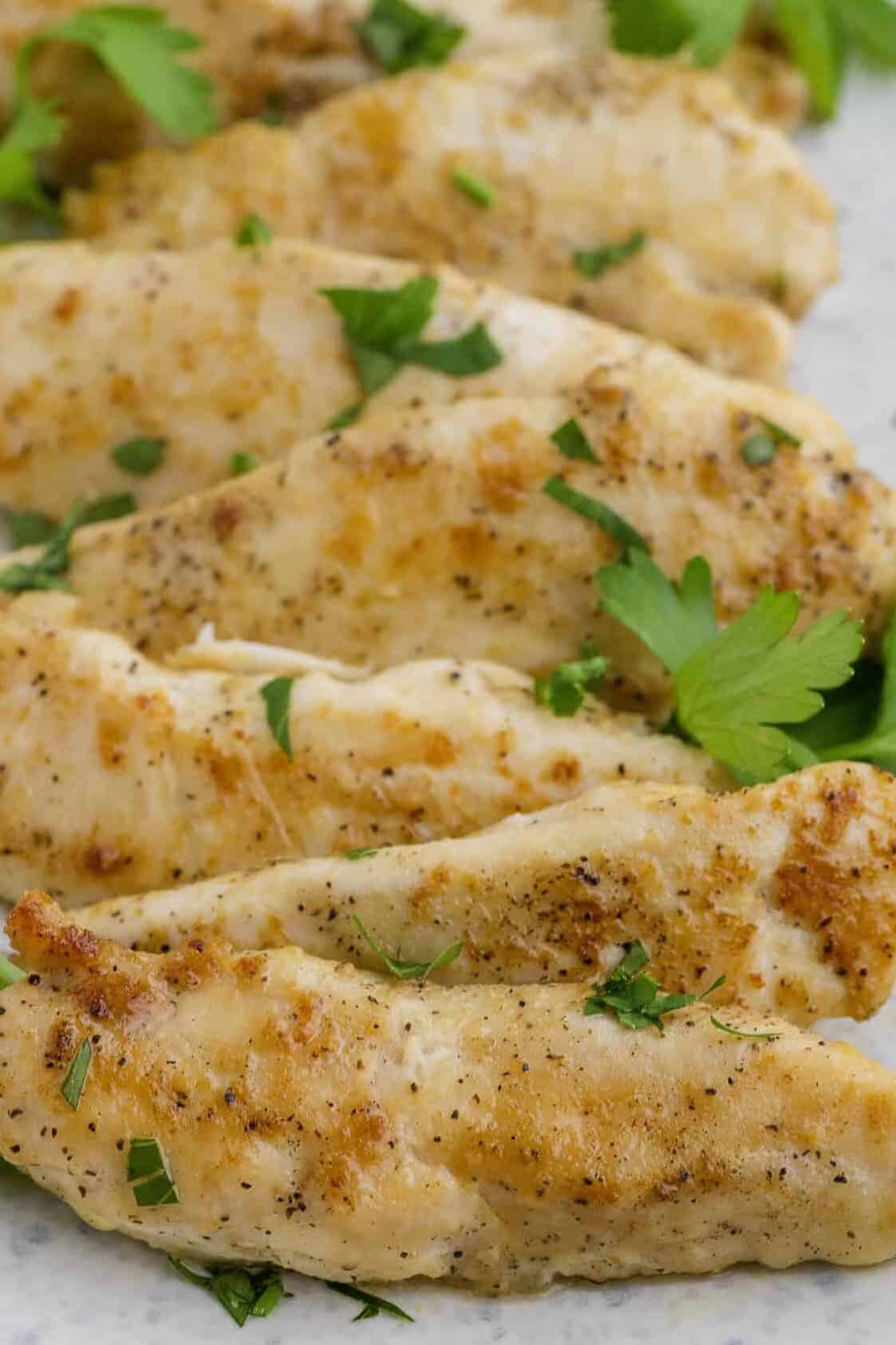 Cooked chicken tenders slices garnished with herbs, arranged on an oval white plate.