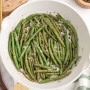 Haricots verts sautés avec du fromage râpé dans une poêle blanche.