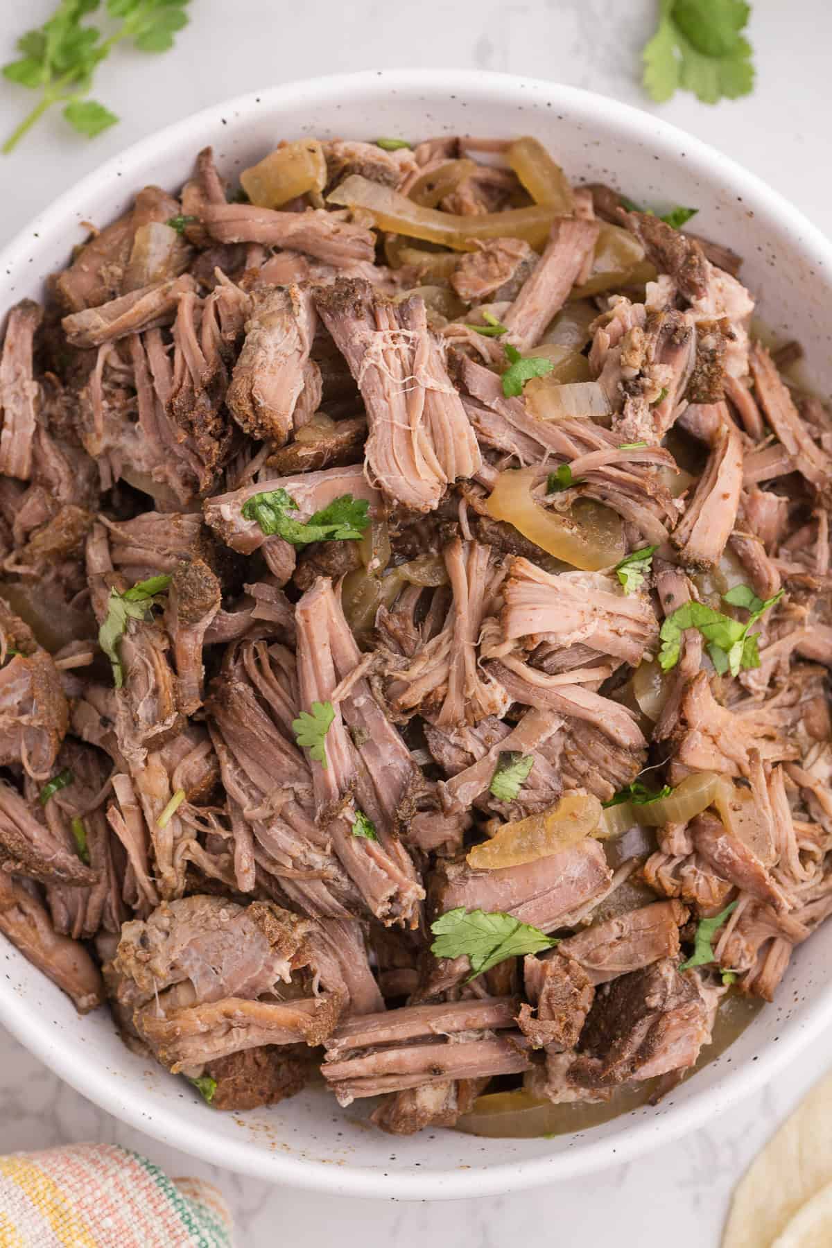 A bowl of shredded beef mixed with cooked onions and garnished with fresh cilantro.