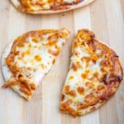 A small pizza with melted cheese and sauce is cut into two uneven pieces on a wooden surface.