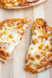 A small pizza with melted cheese and sauce is cut into two uneven pieces on a wooden surface.