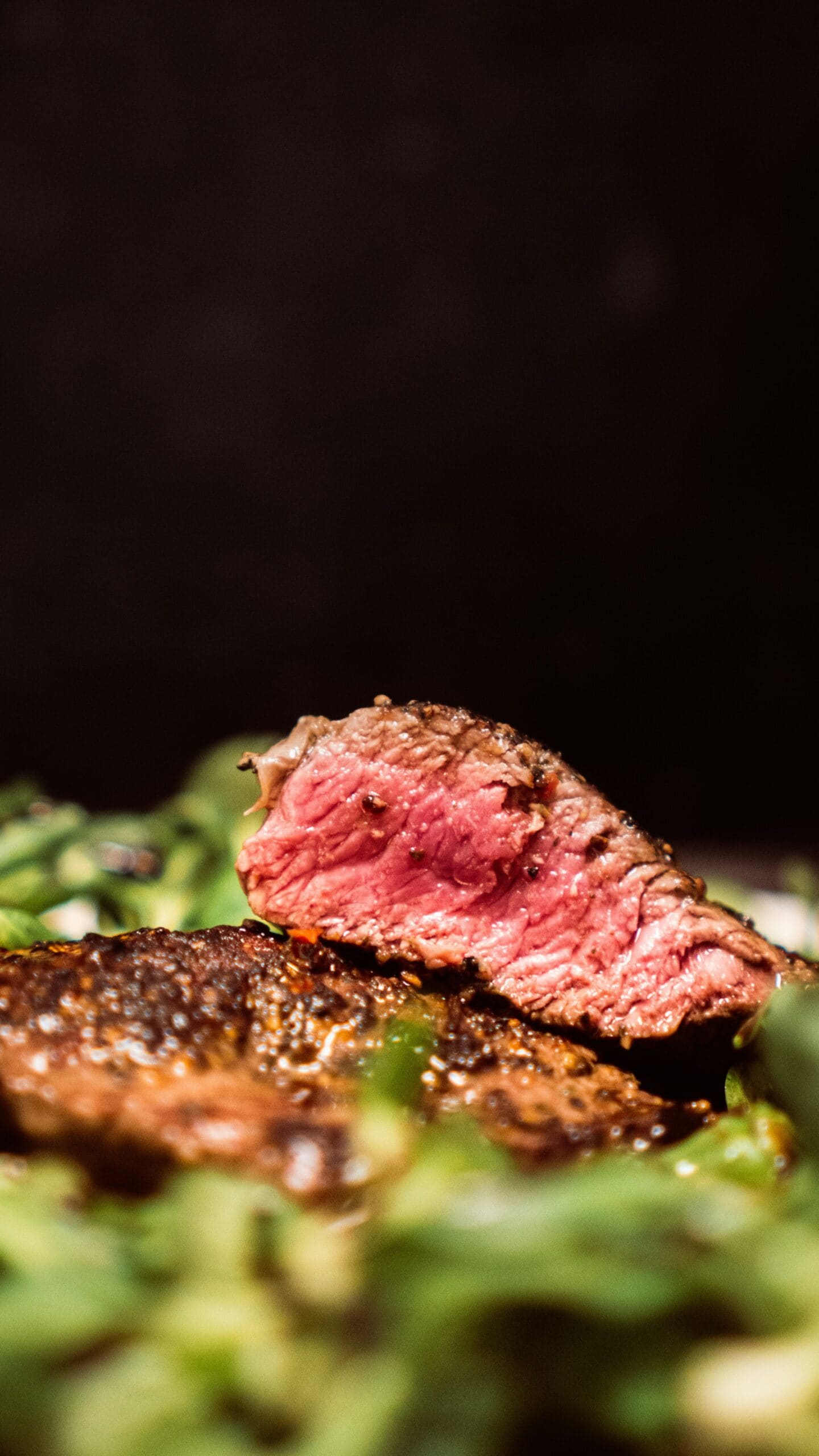 A close-up of sliced medium-rare steak on a bed of greens, showing a seared exterior and a pink, juicy interior.