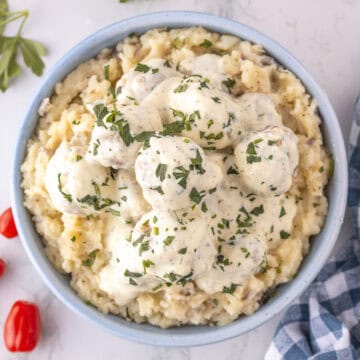 A bowl of mashed potatoes topped with creamy Ranch Chicken Meatballs, covered in sauce and garnished with chopped parsley.