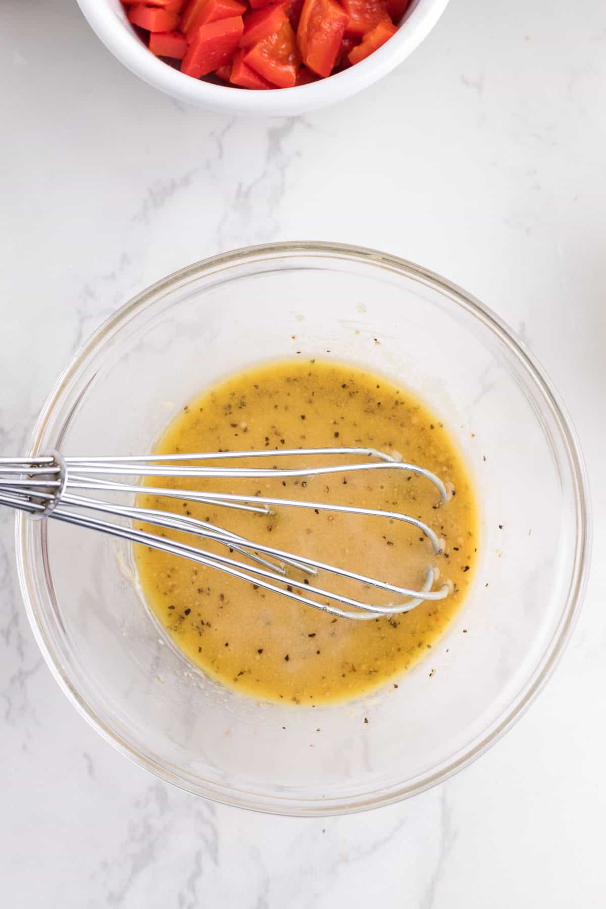 A glass bowl with whisked salad dressing and a metal whisk inside.