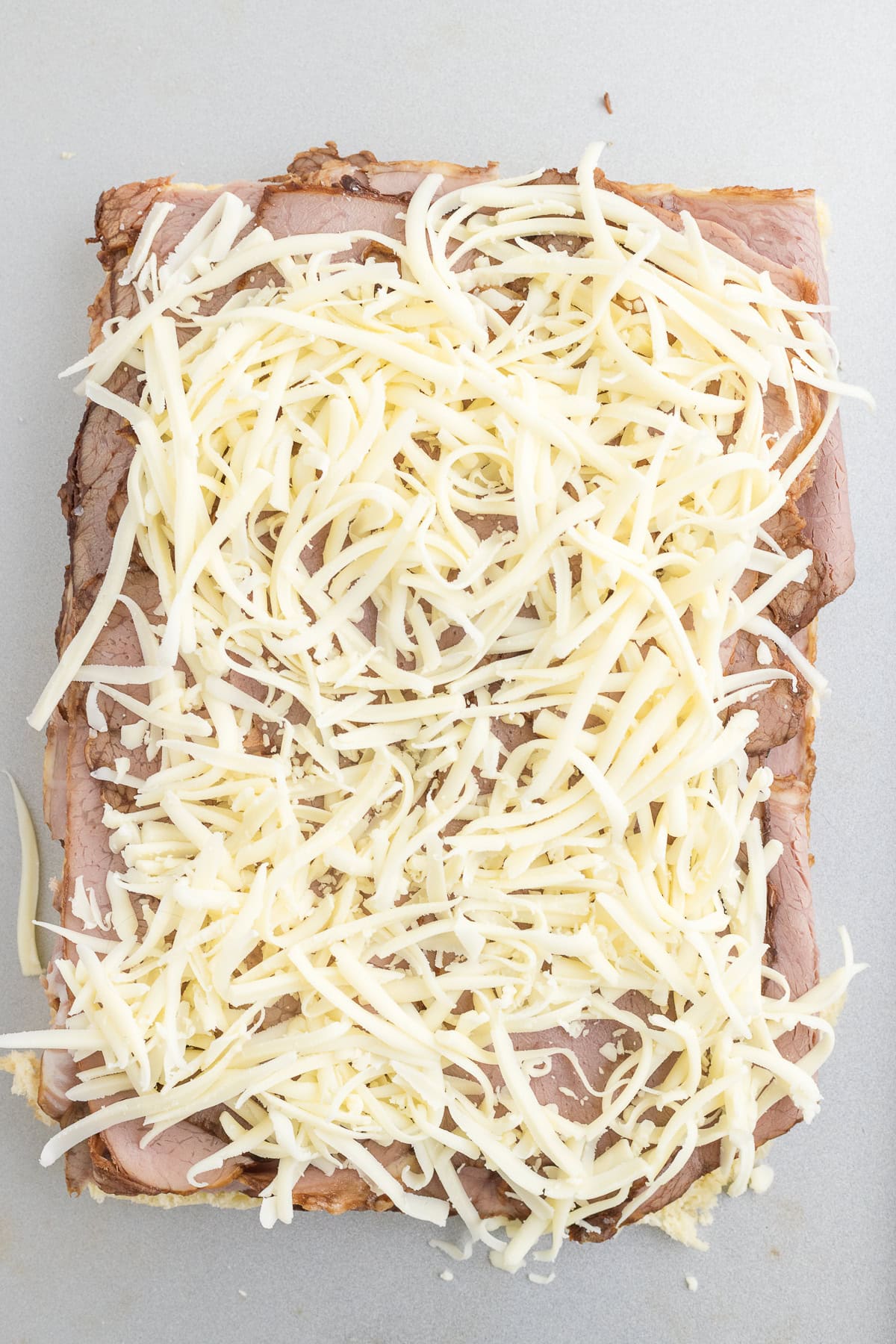 A slice of bread topped with layers of roast beef and a generous amount of shredded cheese on a light surface.