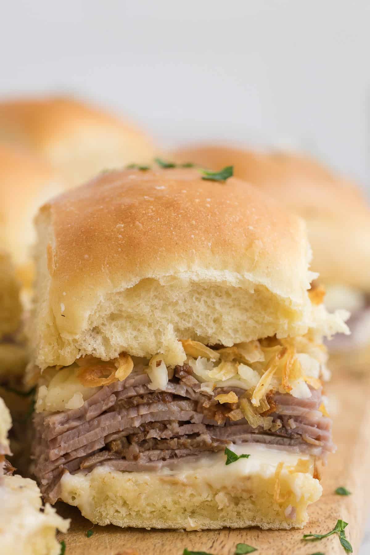A close-up of a sandwich slider with layers of roast beef, melted cheese, and crispy onions on a soft bun, garnished with chopped parsley.