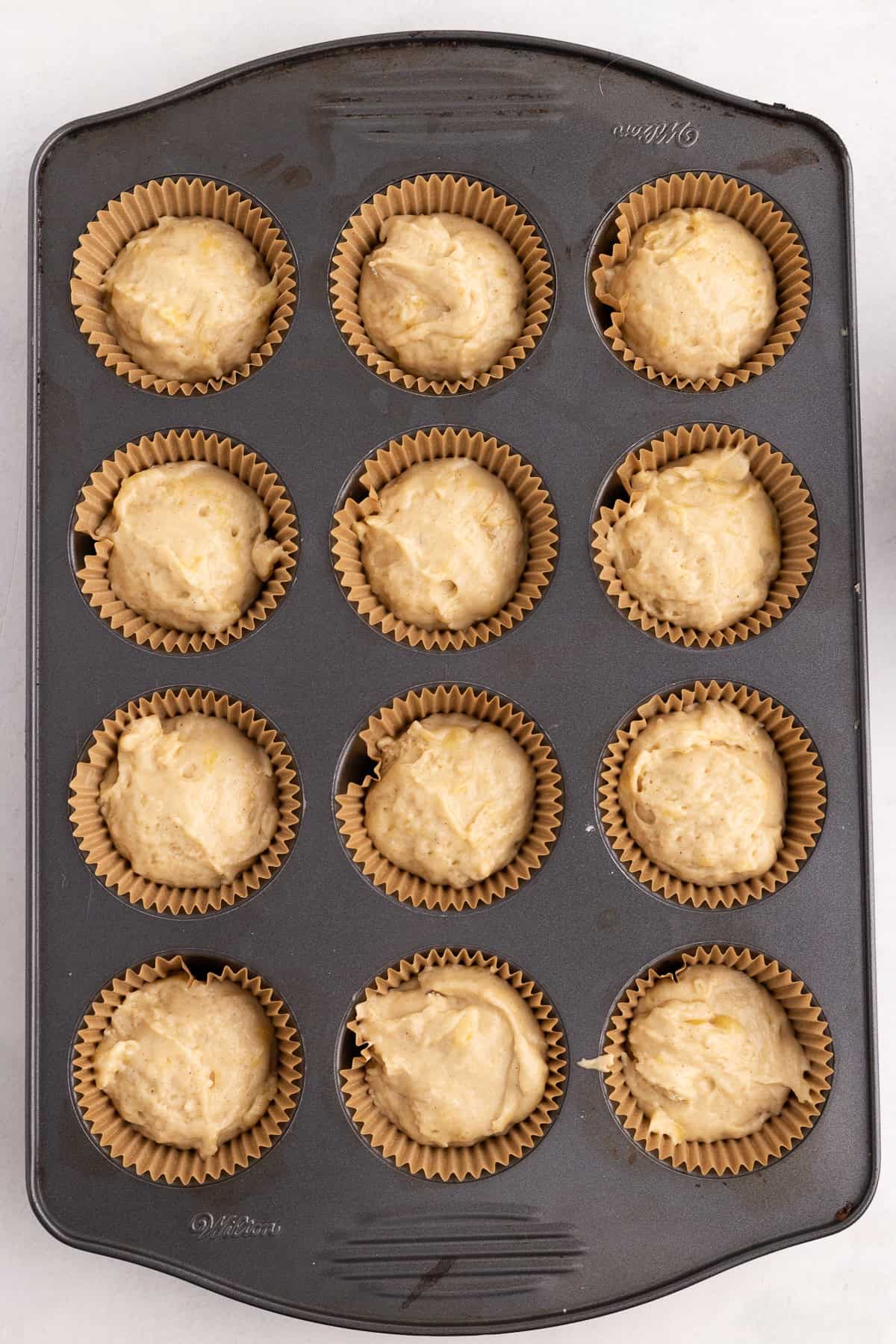 A muffin tin filled with twelve paper liners, each containing unbaked batter.