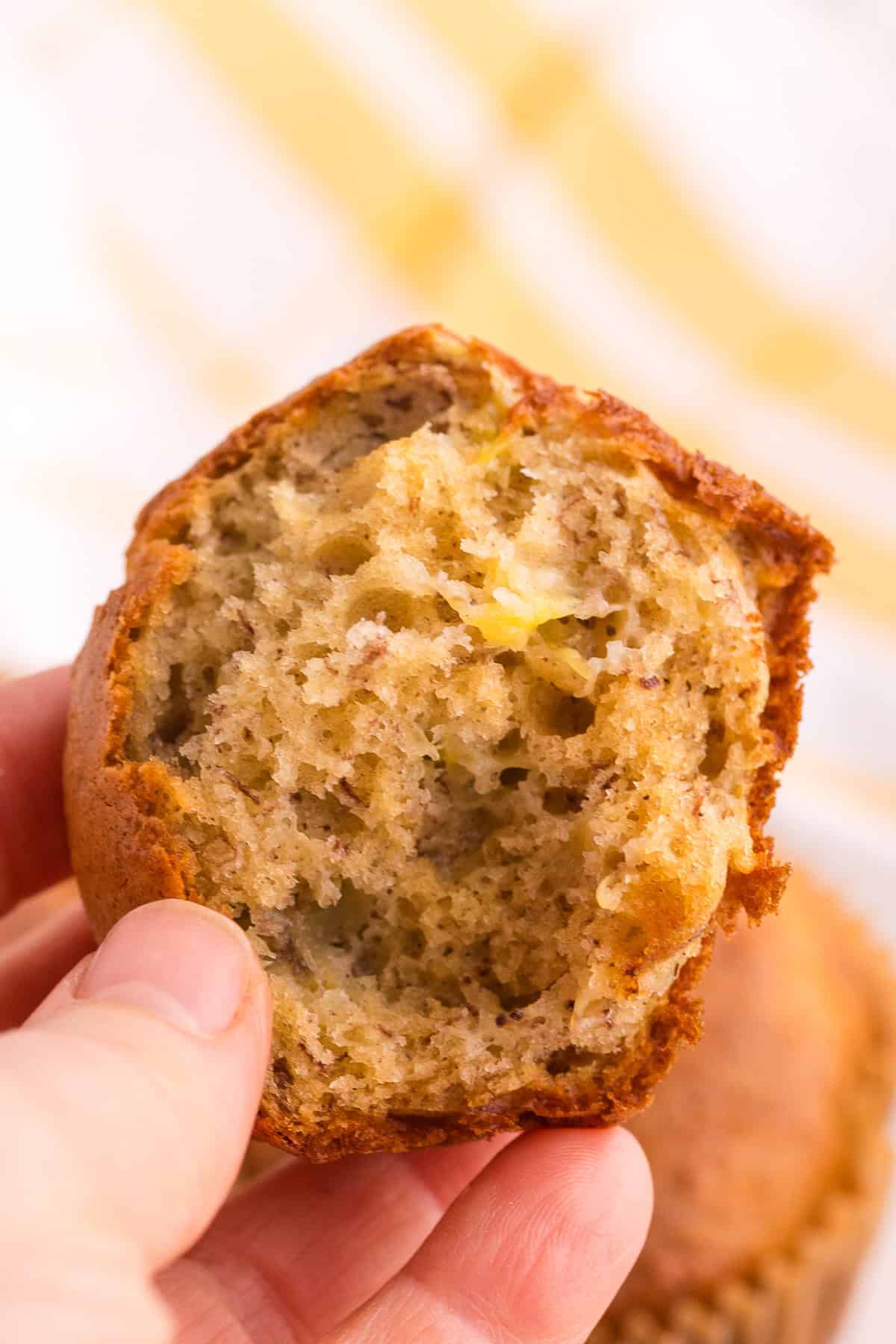 A hand holding half of a banana muffin with a moist and textured interior visible.