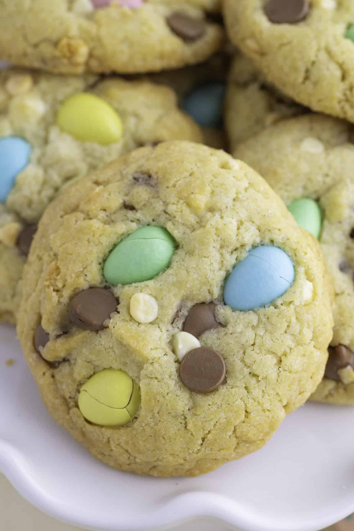 A close-up of a cookie with colorful candy-coated chocolates, chocolate chips, and white chocolate chips on a white plate.