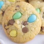 A close-up of a cookie with colorful candy-coated chocolates, white chocolate chips, and milk chocolate chips baked into it.