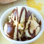 Three scoops of vanilla ice cream in a white bowl topped with chocolate sauce.