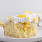 A slice of pineapple poke cake topped with white whipped cream and pieces of pineapple, served on a white plate.