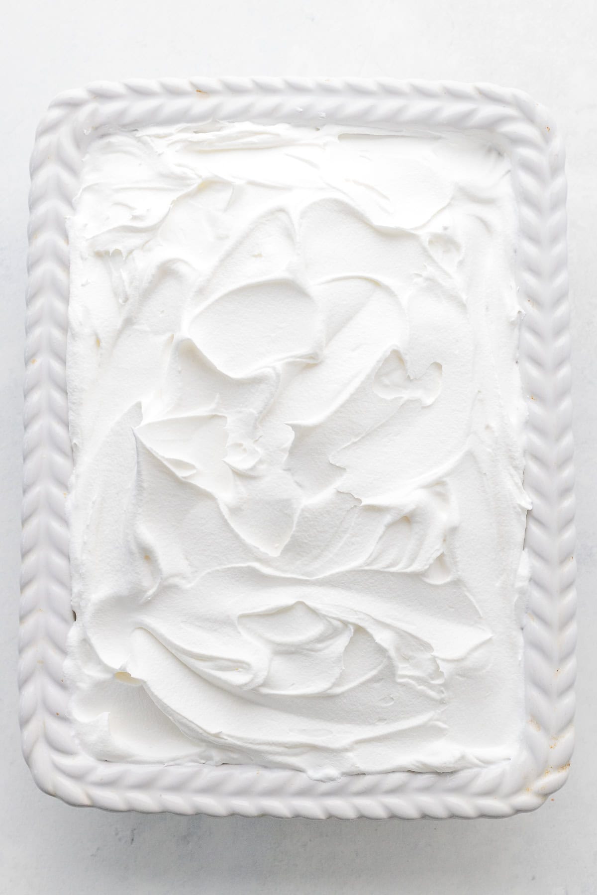 A rectangular white ceramic dish filled with a dessert topped with a thick, smooth layer of whipped cream.