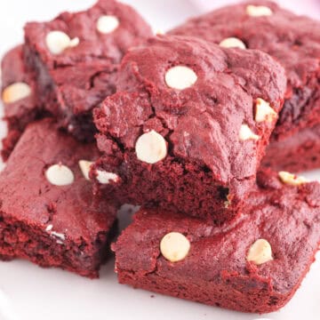 Four red velvet brownies with white chocolate chips are stacked on a white plate.