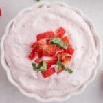 A white bowl filled with pink strawberry mousse, topped with chopped strawberries and fresh green herbs.
