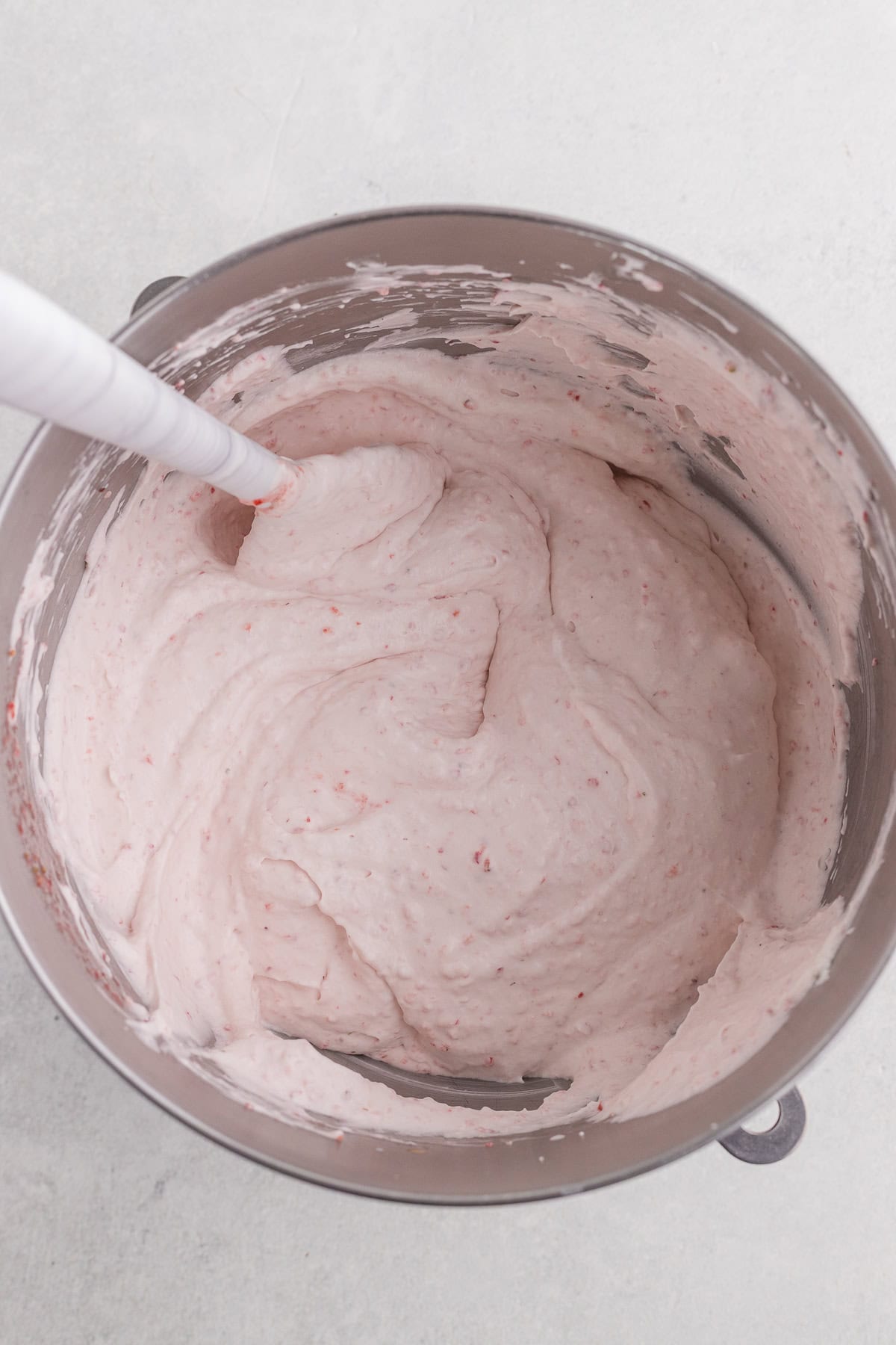 A mixing bowl containing pink strawberry mousse with a spatula resting inside.