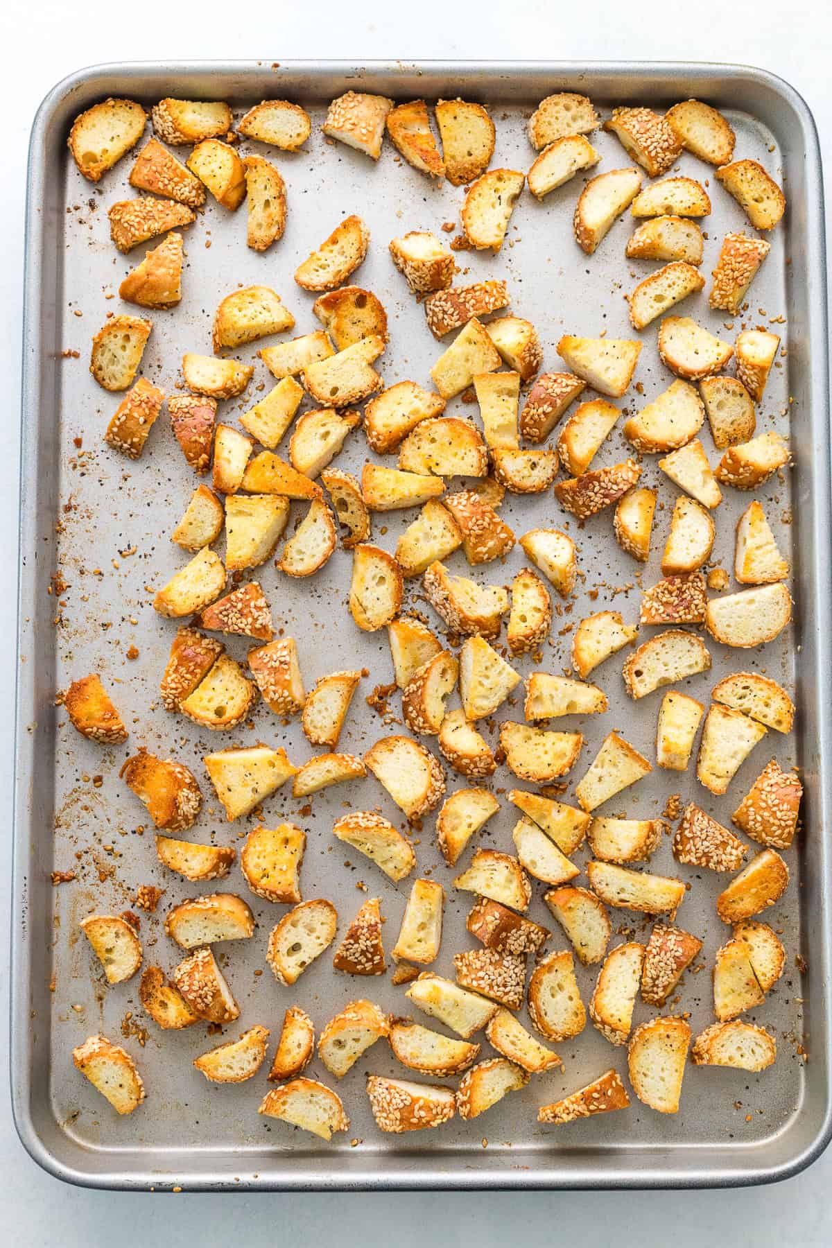 A baking sheet filled with evenly spread, toasted bread cubes coated with seasoning and sesame seeds.