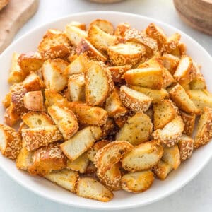 A white bowl filled with golden-brown, sesame-topped bread croutons, cut into bite-sized pieces.