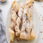 A plate of twisted puff pastry sticks dusted with powdered sugar, arranged on a light-colored oval dish.
