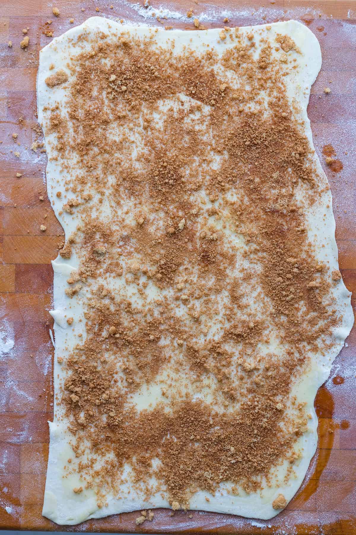 A rectangle of rolled-out dough on a floured surface, topped with an even layer of brown sugar and cinnamon mixture.