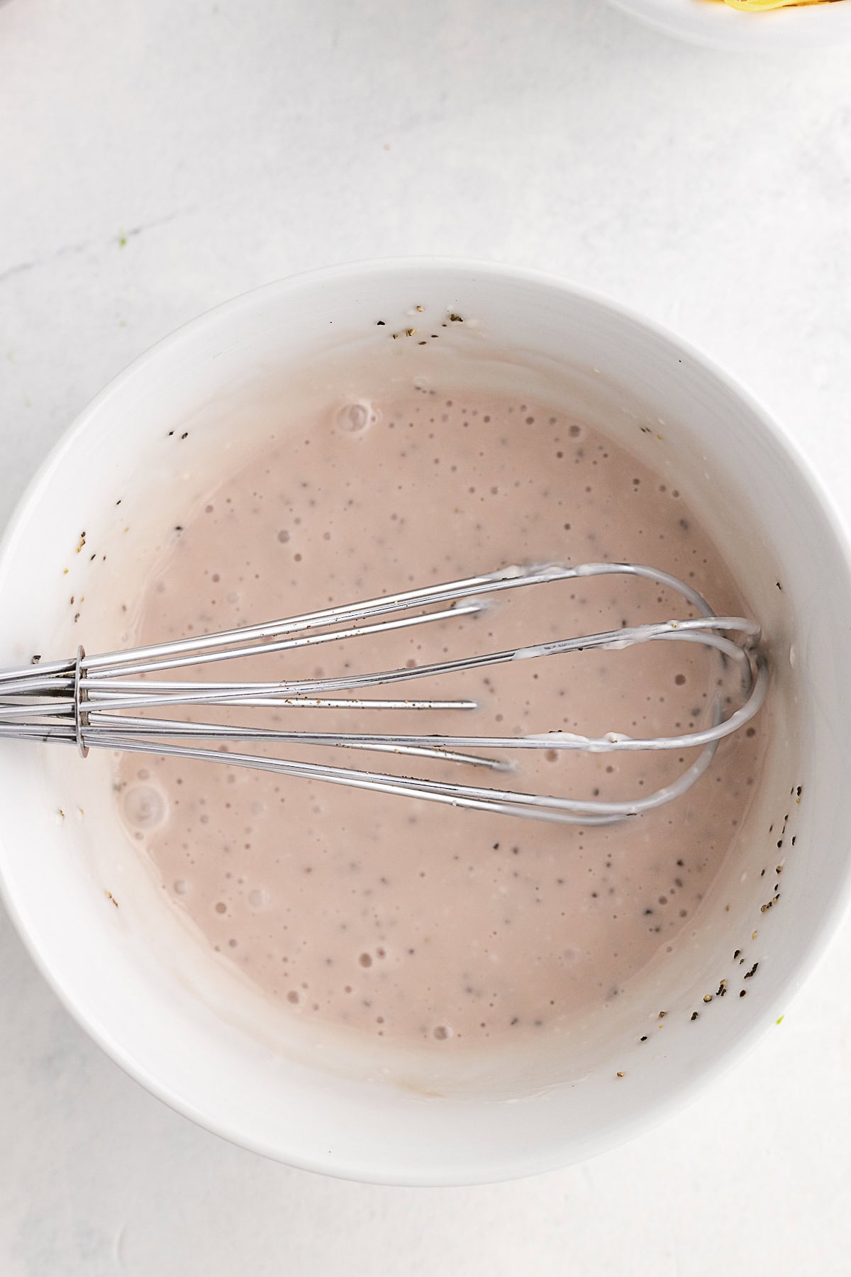 A metal whisk rests in a white bowl filled with dressing.