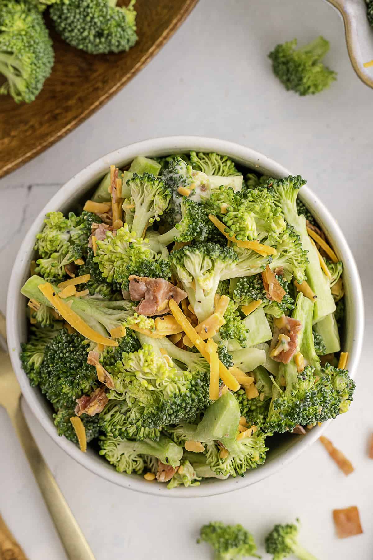 A bowl of broccoli salad with shredded cheddar cheese and pieces of bacon.