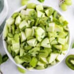 A bowl filled with chopped green fruits including apples, kiwi, grapes, and melon, garnished with fresh mint leaves.