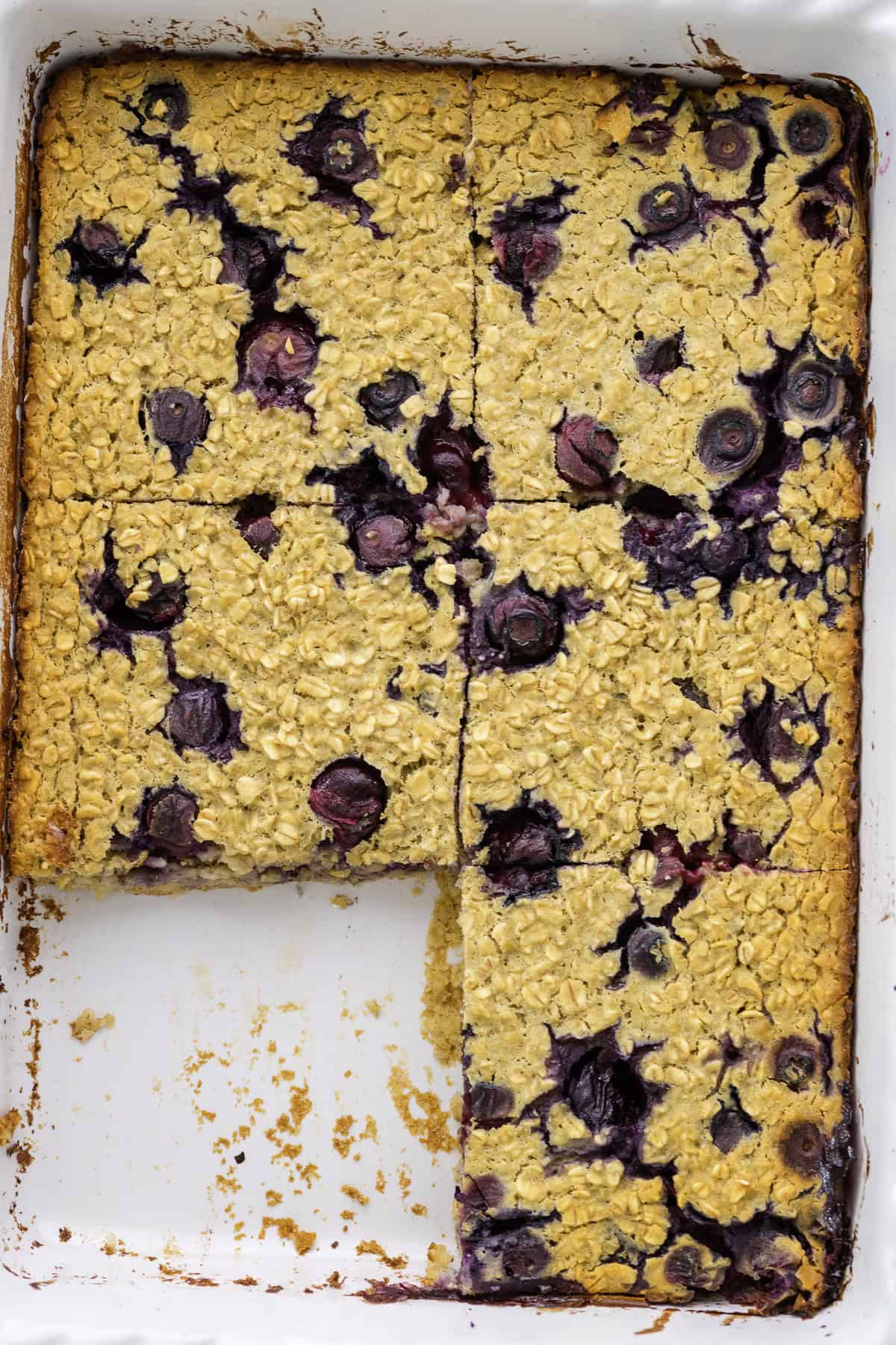 A baked oatmeal dish with blueberries, partially sliced into six pieces in a white rectangular baking pan.