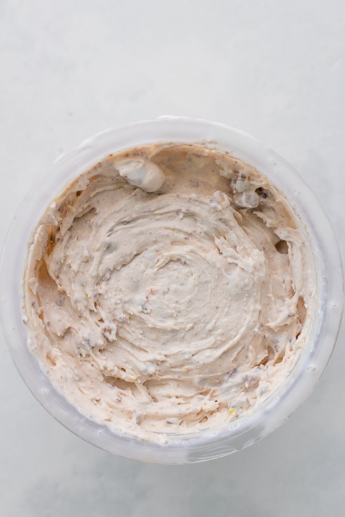 A close-up top view of a container filled with a creamy, speckled ice cream on a light surface.