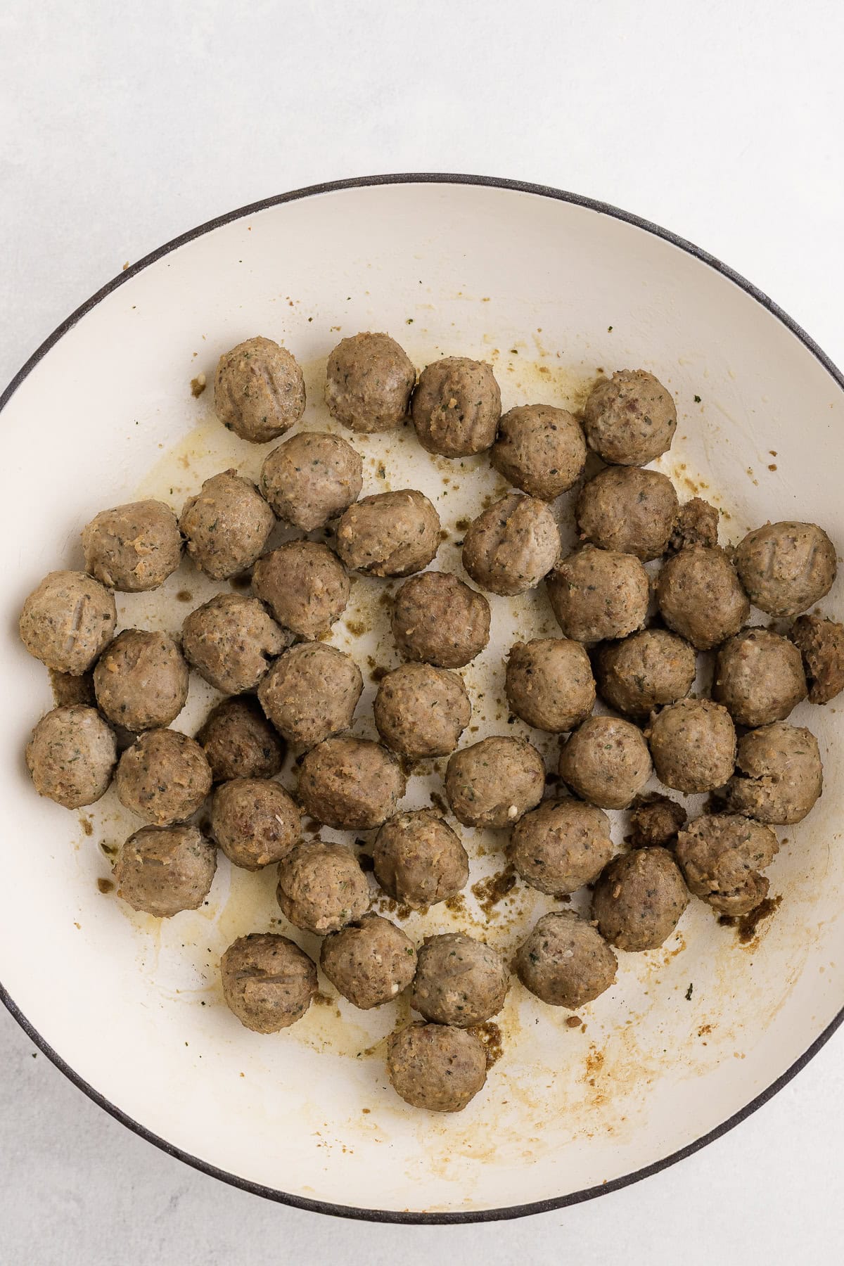 A white pan filled with cooked meatballs, lightly browned and arranged in a single layer on the surface.
