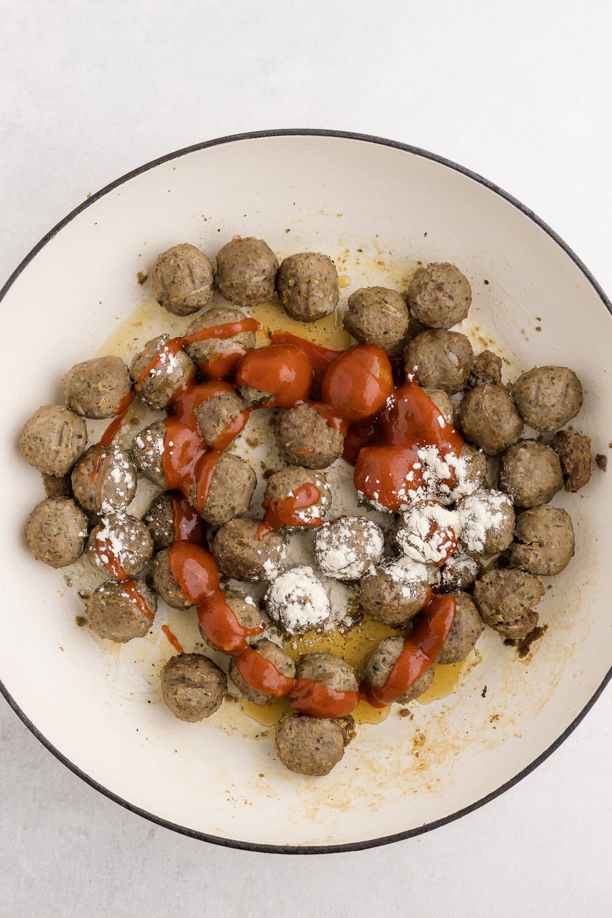 A bowl of cooked meatballs topped with red sauce and garlic powder, with oil visible at the bottom.