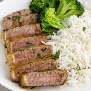 Sliced medium-rare steak served with steamed broccoli and white rice on a white plate.