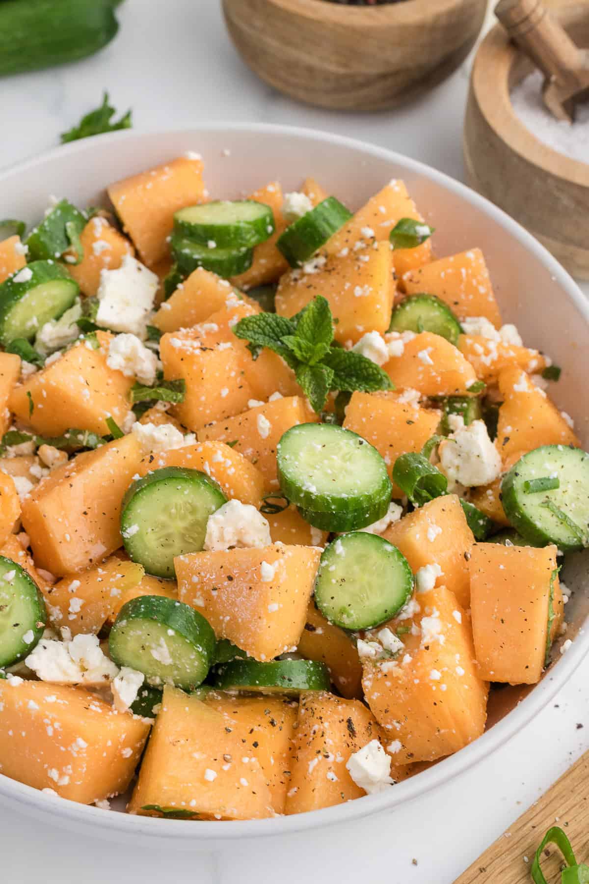 A bowl of salad with cubed cantaloupe, sliced cucumber, crumbled feta cheese, black pepper, and mint leaves.