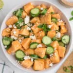 Bowl of salad with cantaloupe chunks, cucumber slices, crumbled feta cheese, black pepper, and mint leaves on top.